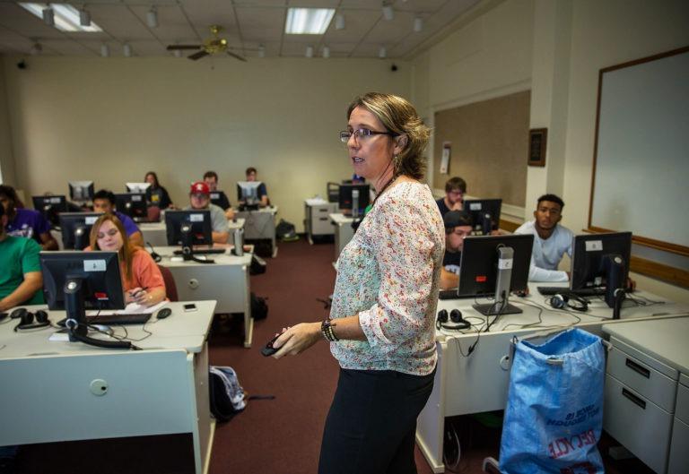 Kinesiology professor standing in front of class lecturing and pointing to white board